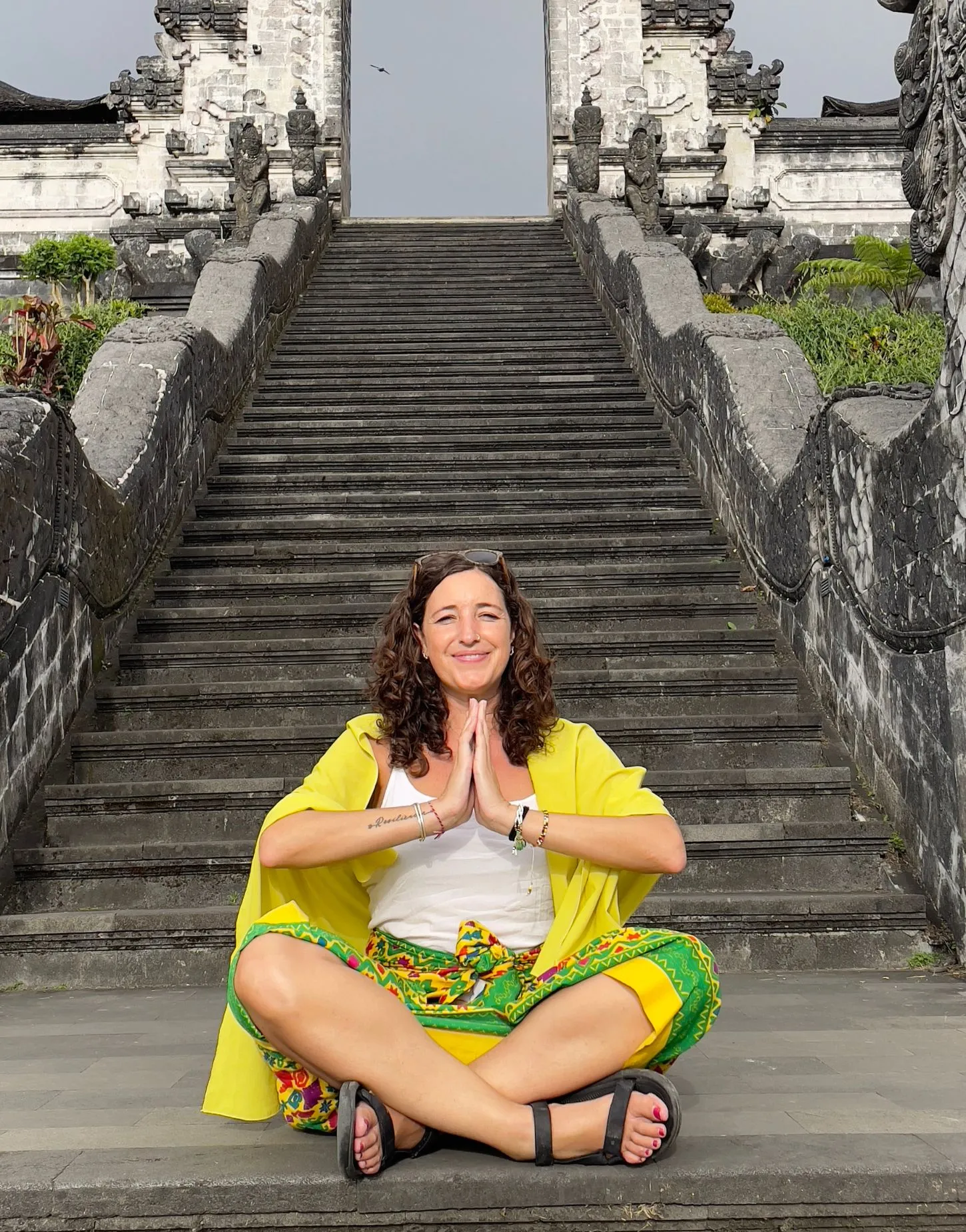 Meri, fundadora de Alas en la Mochila, sentada en posición de meditación frente a las escaleras de un templo tradicional en Bali.